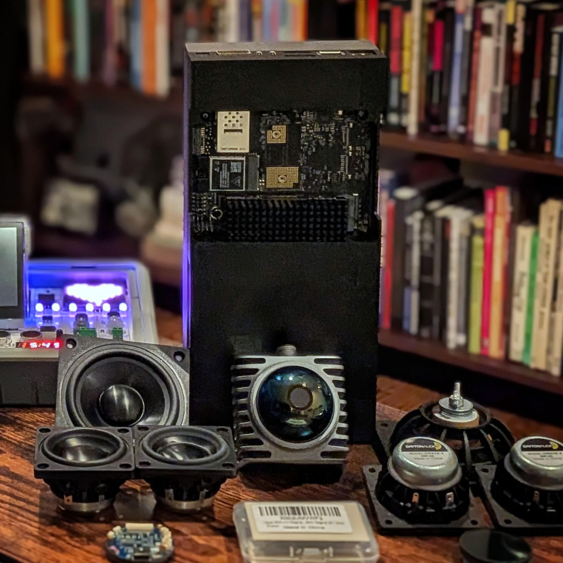 Angel's hardware laid out on a wood table: the Jetson AGX Thor in its black case standing upright, a camera module, and several speaker drivers.