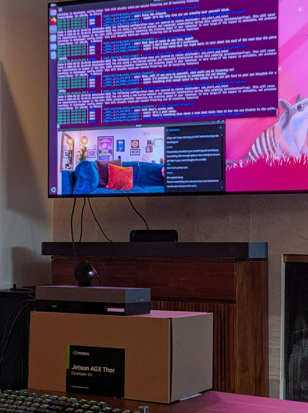 Angel running on the TV: a terminal log on top, and below it her live camera view of the living room next to a chat panel marked LISTENING. The Jetson AGX Thor box sits on a stand under the screen with a webcam on top.