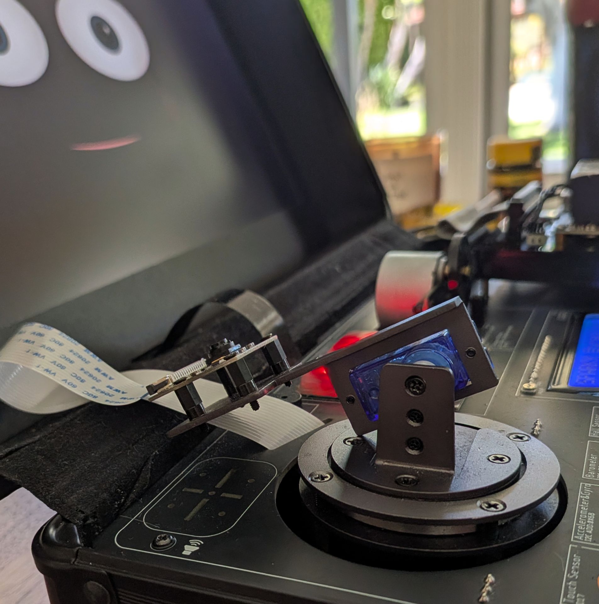 Sparky's camera gimbal folded flat for shutdown: the camera arm tilted all the way back against the deck beside the blue tilt servo, with Sparky's grinning face on the screen behind it.