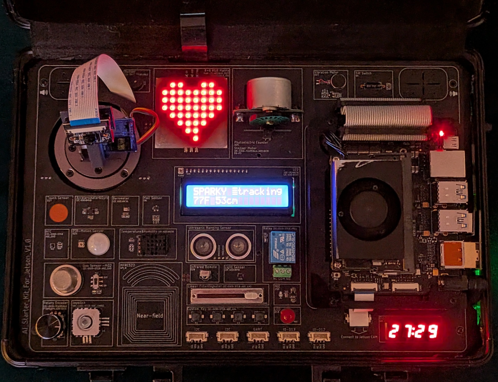 Top-down view of Sparky's open case showing the LCD reading SPARKY tracking 77F 53cm, glowing LED heart matrix, and all integrated sensors